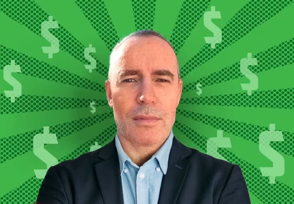 A middle-aged man in a dark blazer and blue shirt against a green background with dollar signs radiating outward.